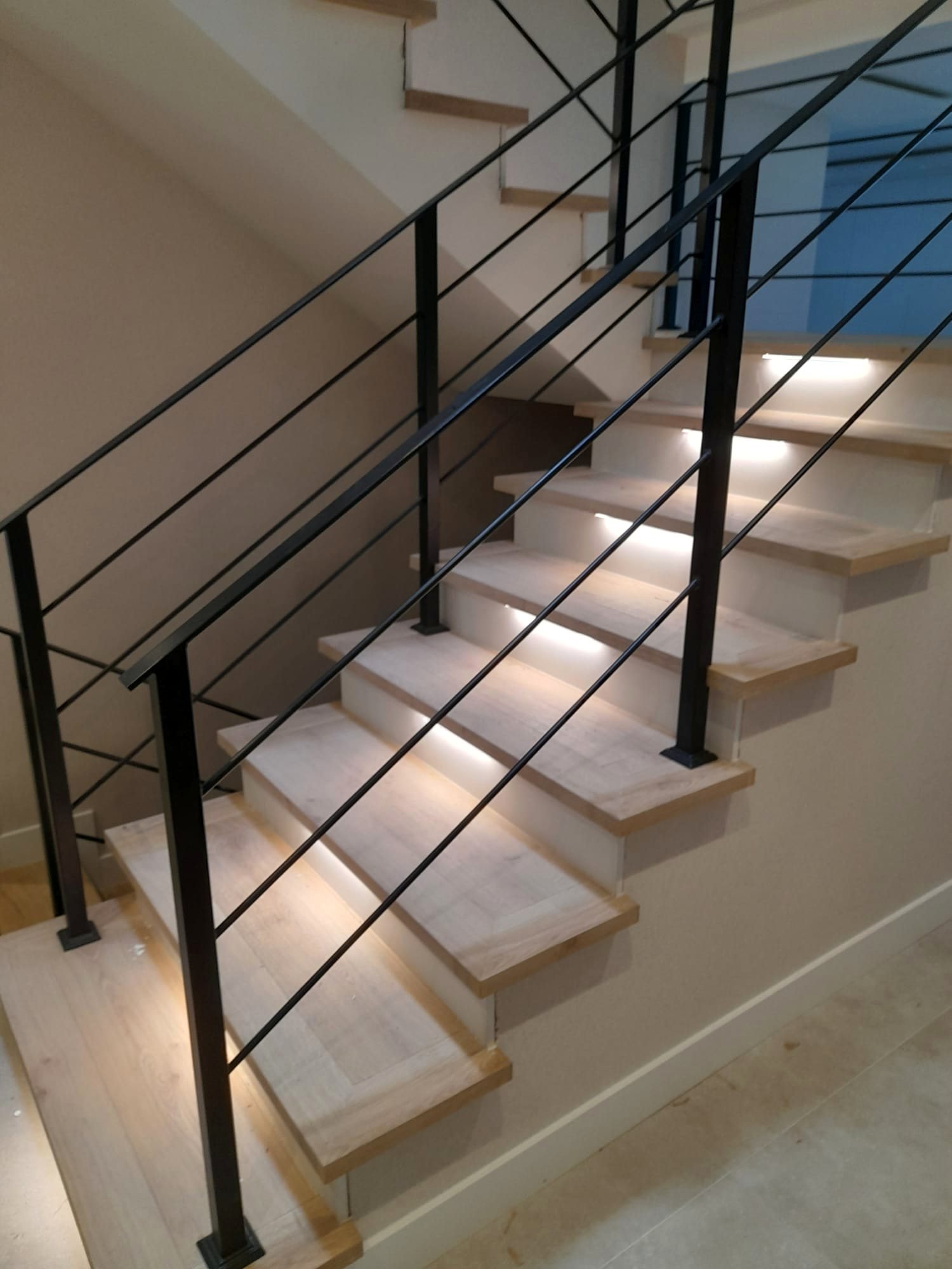 Escalera de madera clara con barandilla metálica negra